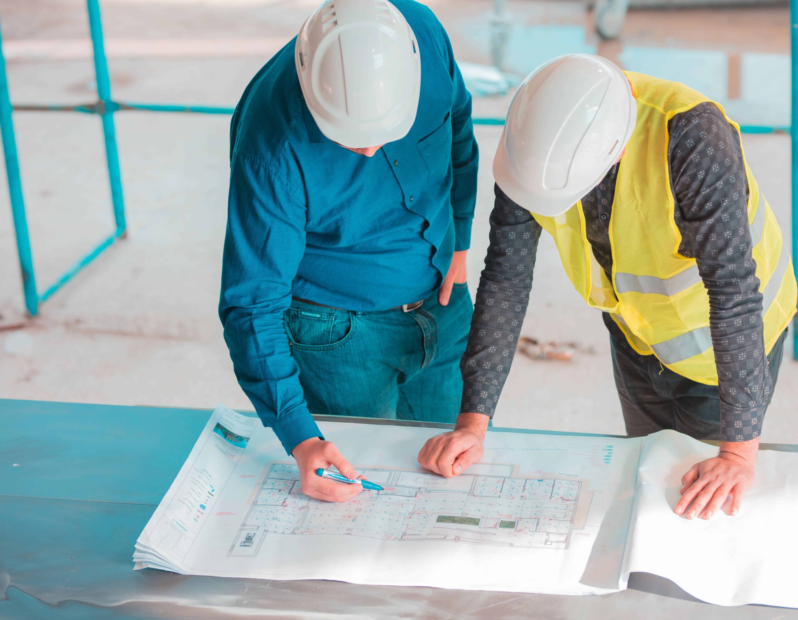 Construction team in safety helmets examining blueprint on site for subsurface utility engineering (SUE) mapping and transportation project coordination.