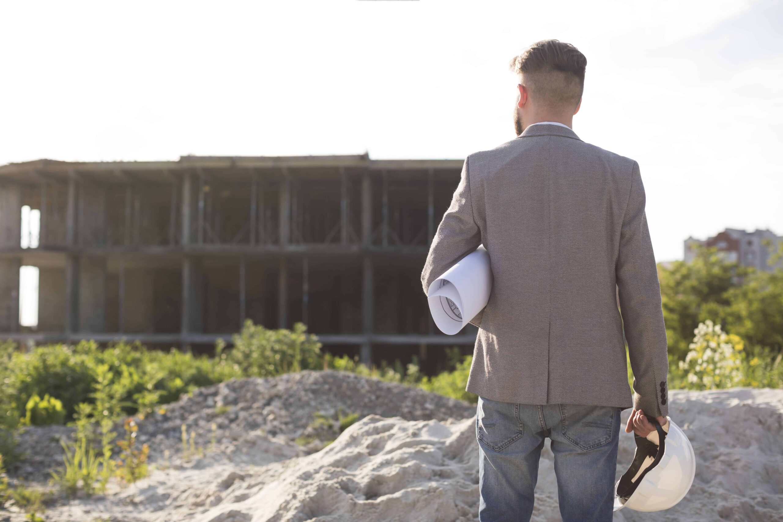 Engineer holding blueprint and hard hat at construction site for private utility locating of water, gas, and electrical lines.