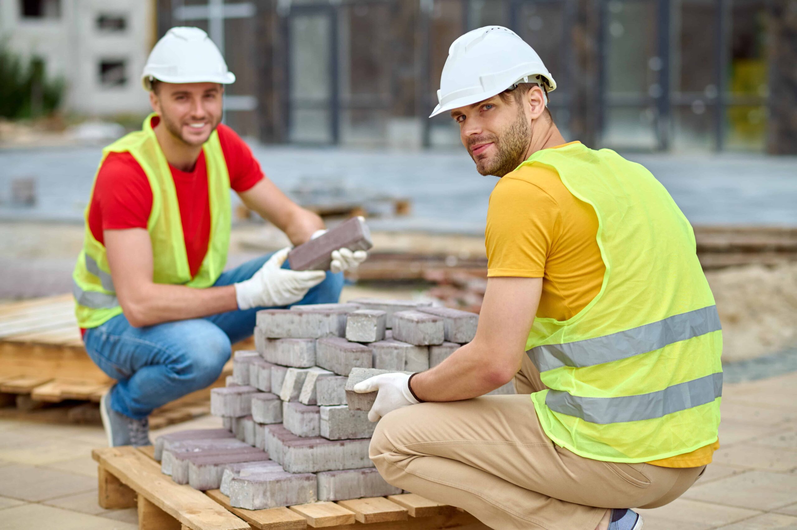 Construction workers in safety helmets and vests preparing site with stacked bricks for trenching, excavation, and underground utility locating.