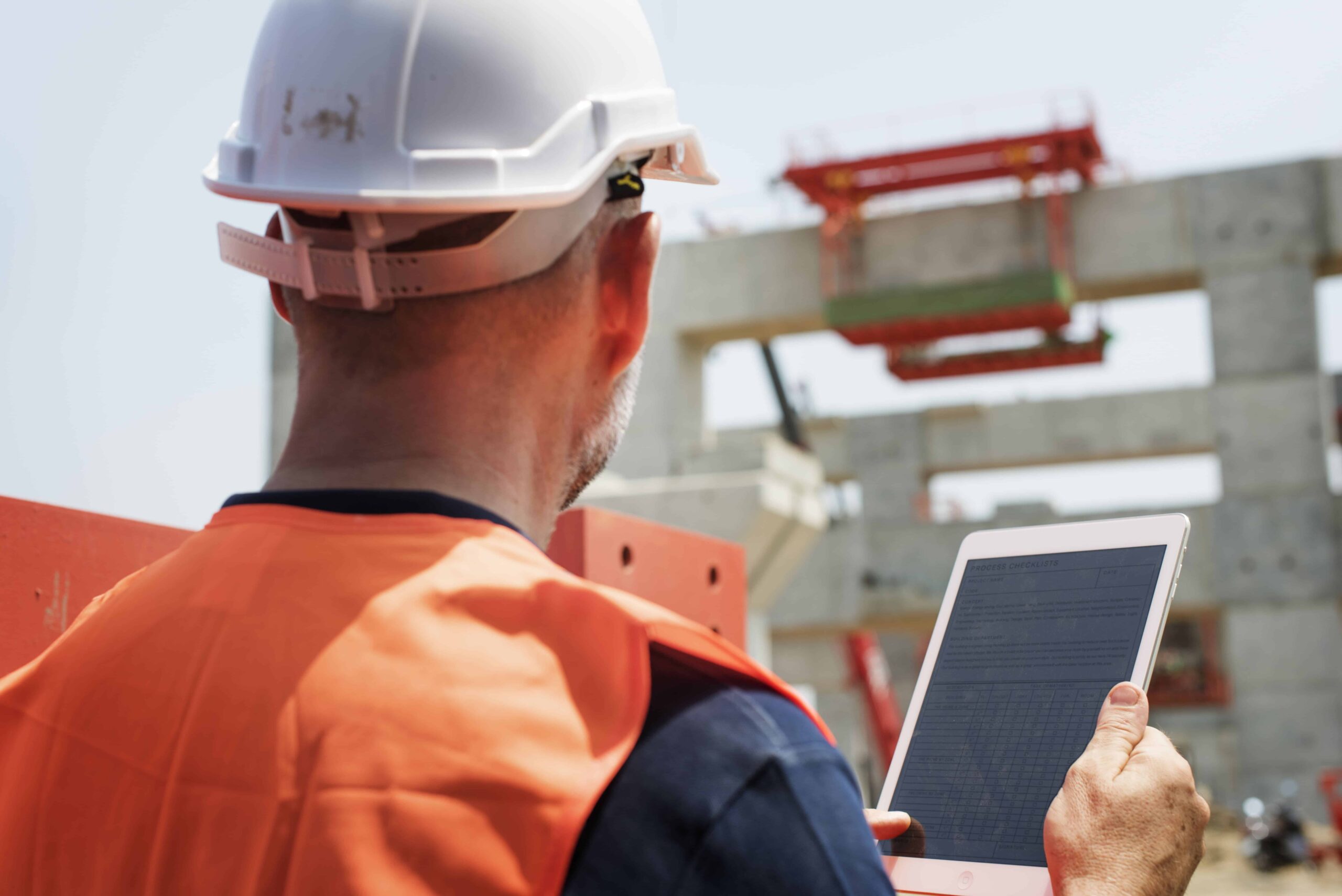 Construction worker in orange safety vest and hard hat using tablet for concrete scanning to detect rebar, post‑tension cables, conduits, and plumbing lines.