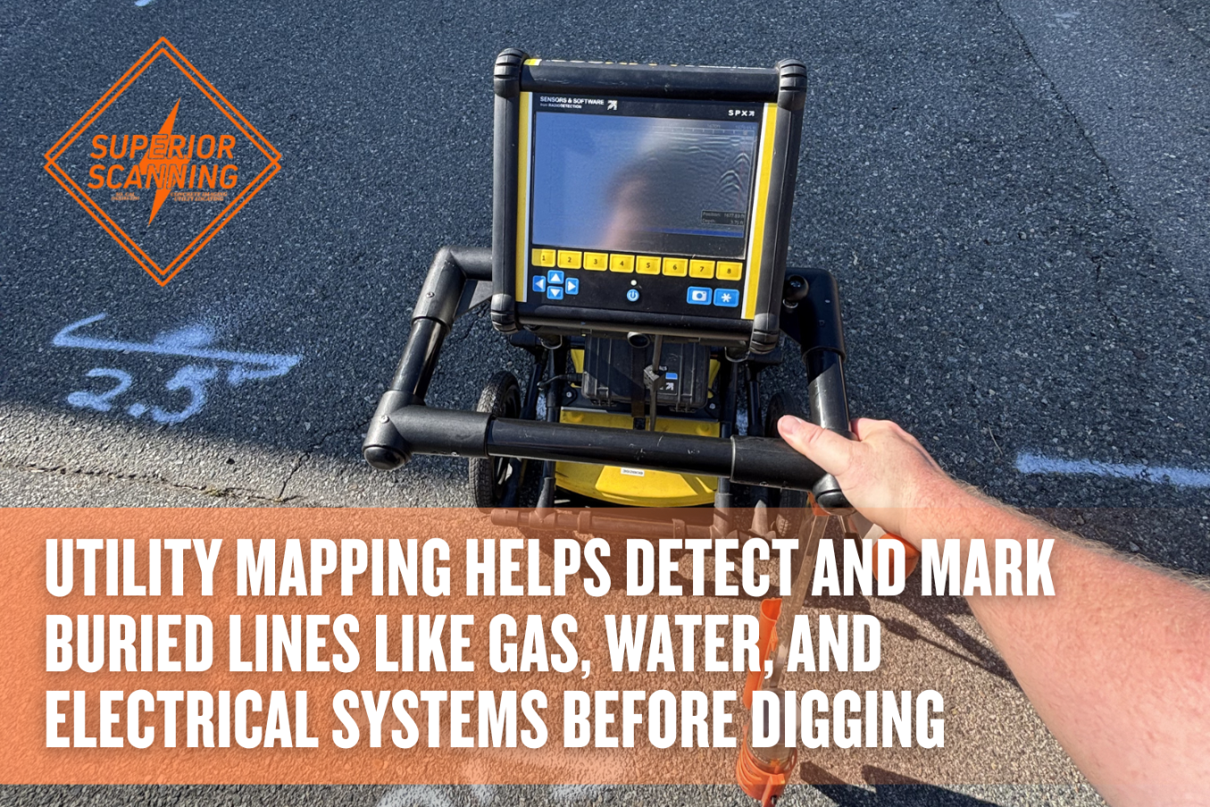 A person pushes a ground penetrating radar unit across an asphalt surface marked with white spray paint measurements.