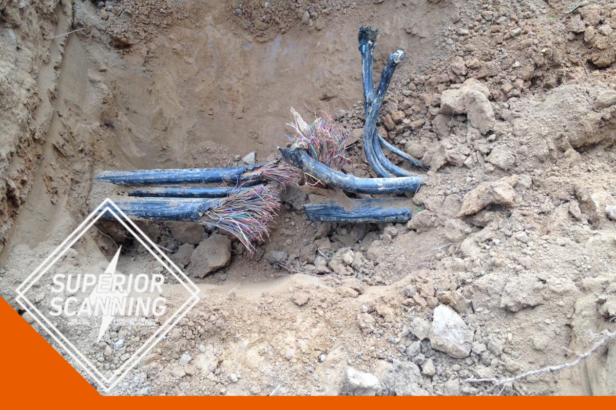 Damaged buried communication cables with exposed colored wires inside a dirt trench on a construction site.