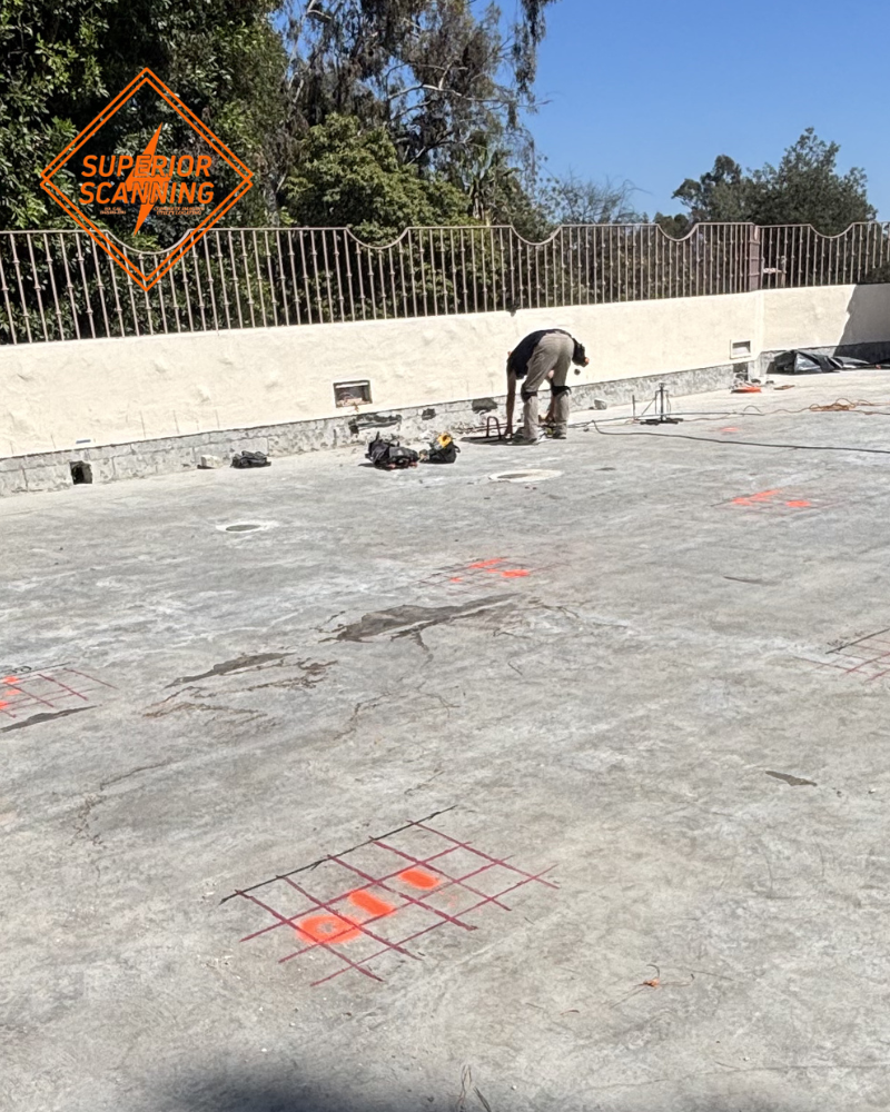 A wide view of a large outdoor concrete slab with multiple red grid markings, showing the results of scanning for post tension cables across a large structural deck.