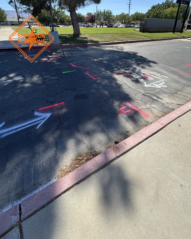 Asphalt and sidewalk with red, green, white, and blue utility markings for comparing private utility locating and 811 public mark-outs.