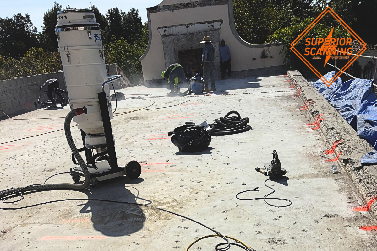 Concrete coring construction site with workers operating cutting equipment and industrial dust collection system on flat concrete surface.