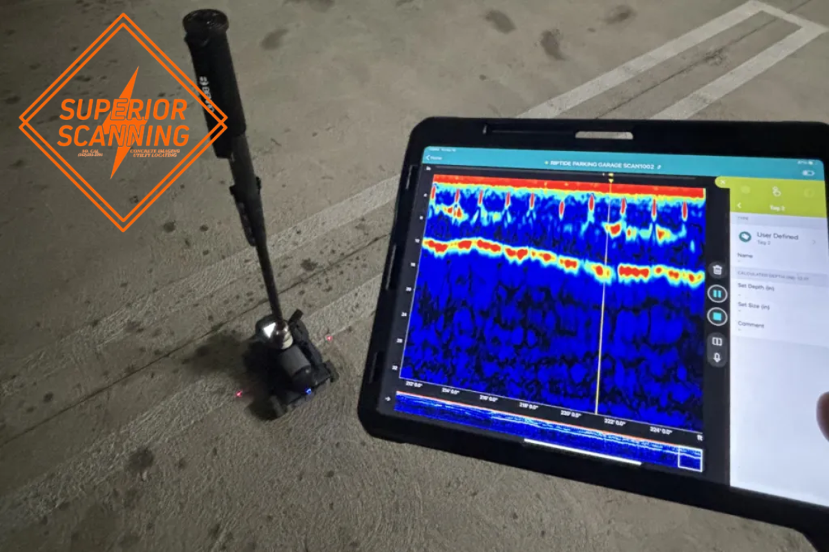 A concrete scanning device with a tablet displaying a heatmap scan of underground structures on a concrete surface.