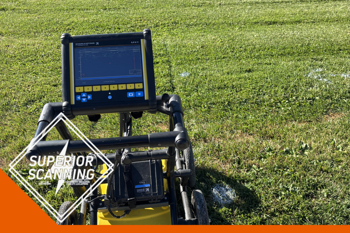 A yellow and black ground penetrating radar unit sits on a green grassy field with a digital display screen showing data.