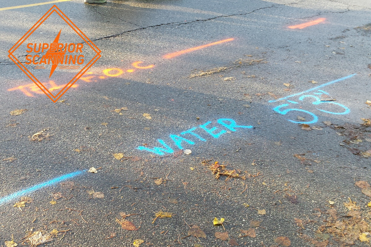 Sewer line locating markings painted on asphalt beside ground-penetrating radar equipment.