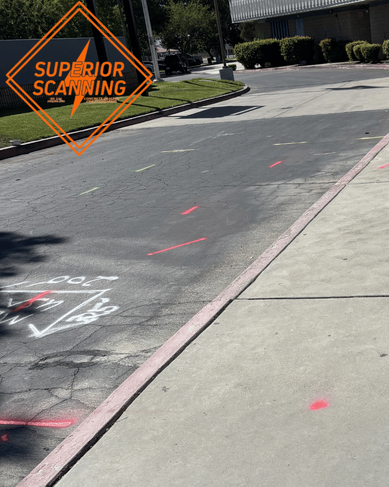A paved walkway and asphalt road marked with red and green spray paint dots and lines, leading to a modern building with a curved facade.