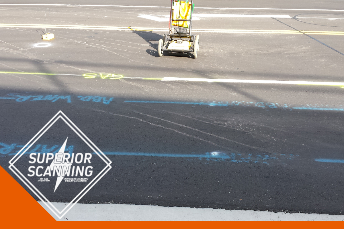 A utility cart is on an asphalt road with painted markings indicating utility lines for water, gas, and other services.
