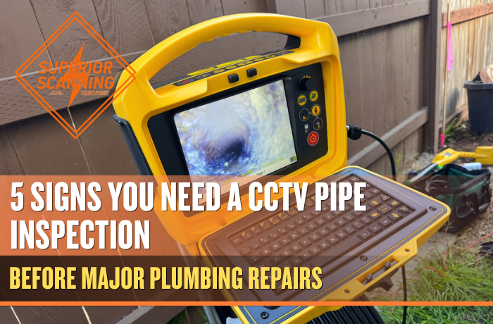 A yellow drain inspection camera with a screen displaying a view inside a pipe, a keyboard, and a coiled cable is set up outdoors near a wooden fence.